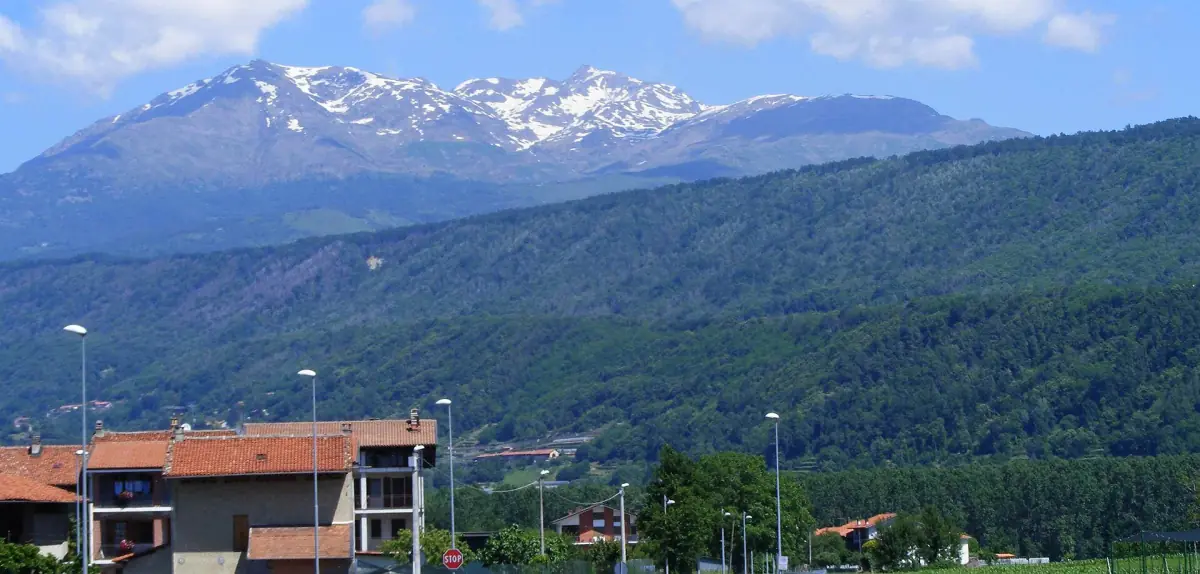 Il Mombarone innevato sopra una valle verde e un paese