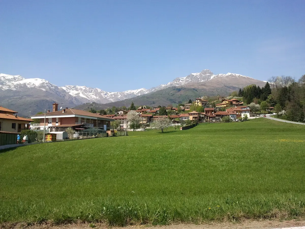Paese prealpino vicino a Biella con cime innevate dietro un prato verde