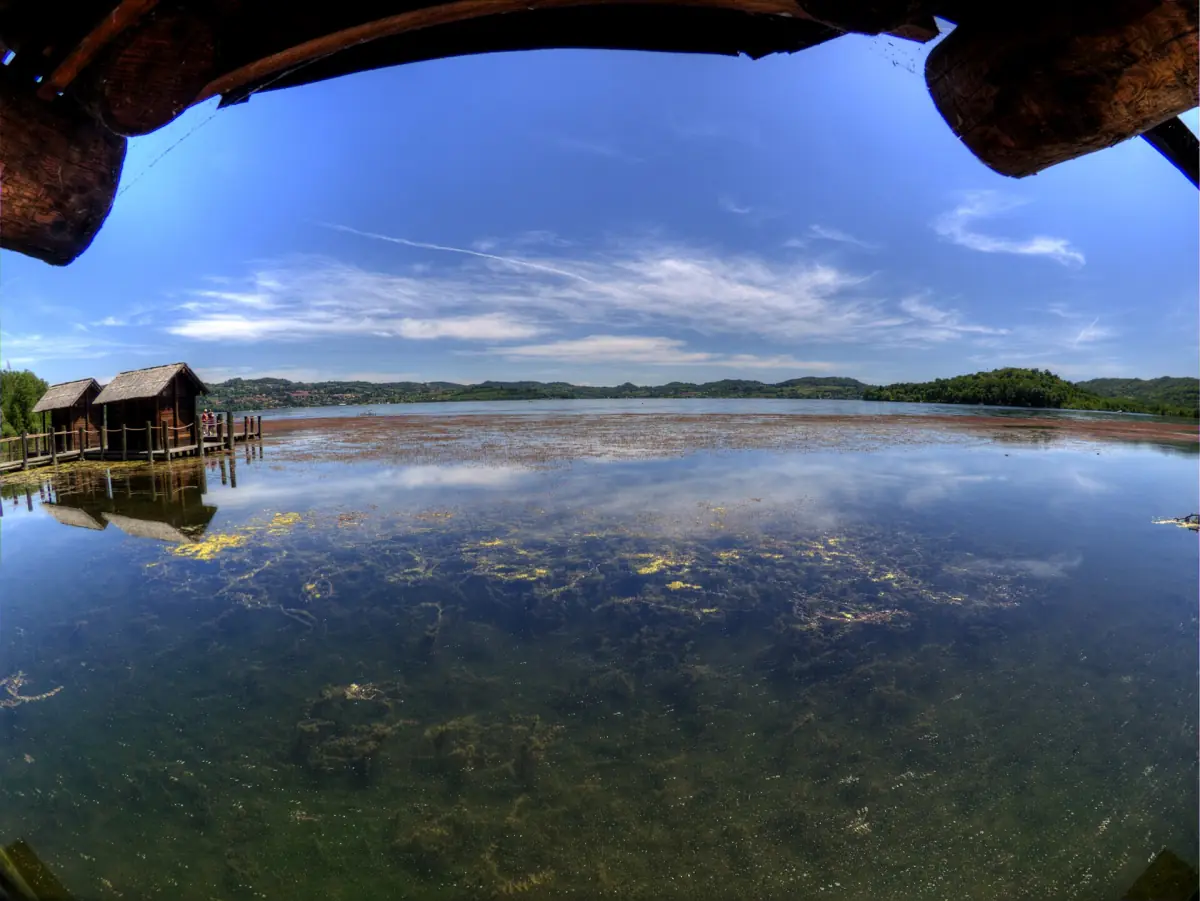 Capanne su palafitte in legno riflesse nell'acqua bassa del lago presso Azeglio